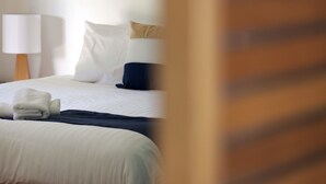 Camera d'albergo con un letto, cuscini, una lampada e un asciugamano piegato sul letto.