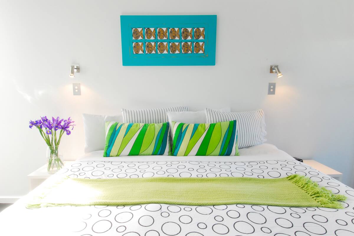 A neatly arranged bedroom with a bed, pillows, a blanket, and a wall art piece.