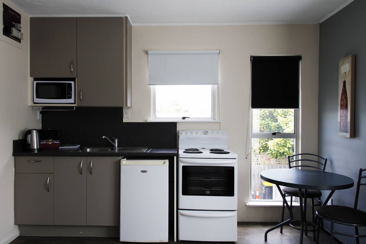 Cocina compacta con refrigerador, microondas, estufa y una mesa de comedor con sillas.