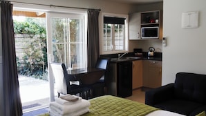 A room with a bed, a desk, a chair, a kitchenette, and a view of the outdoors. - Cranford Cottages And Motel (Christchurch)