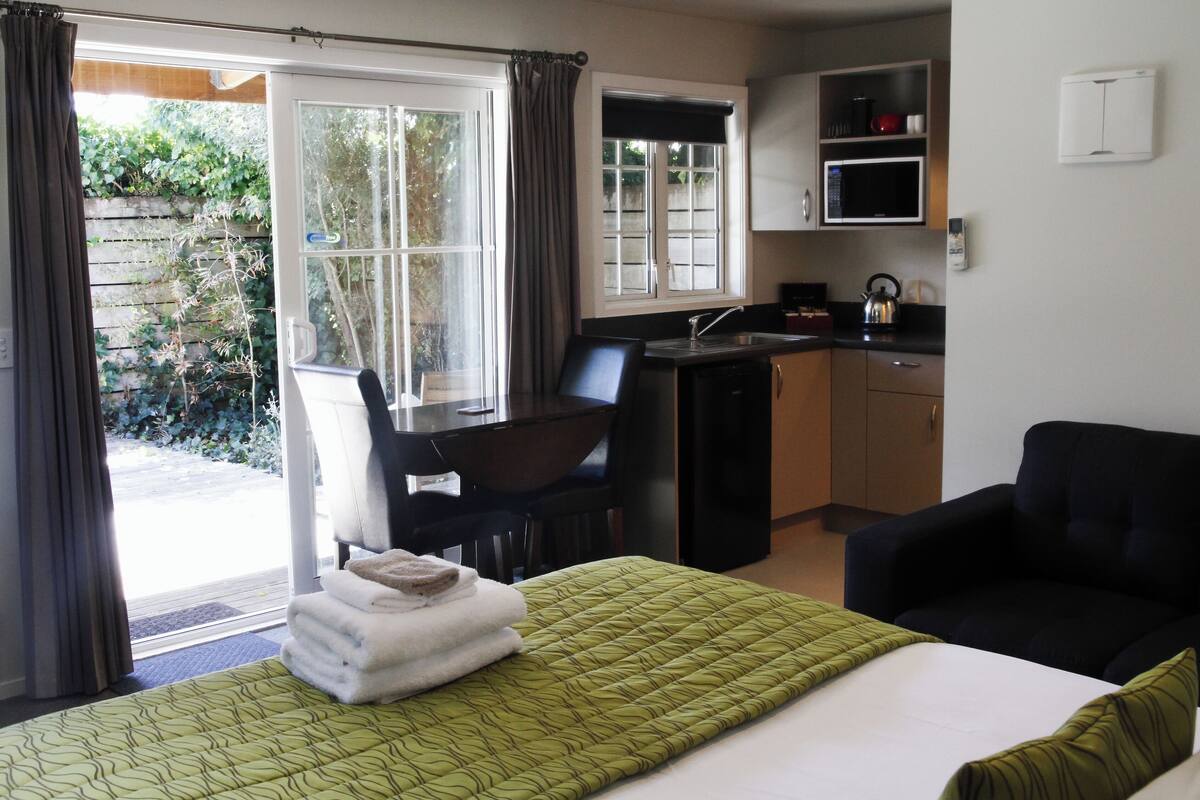 Una habitación con cama, escritorio, silla, kitchenette y vistas al exterior.