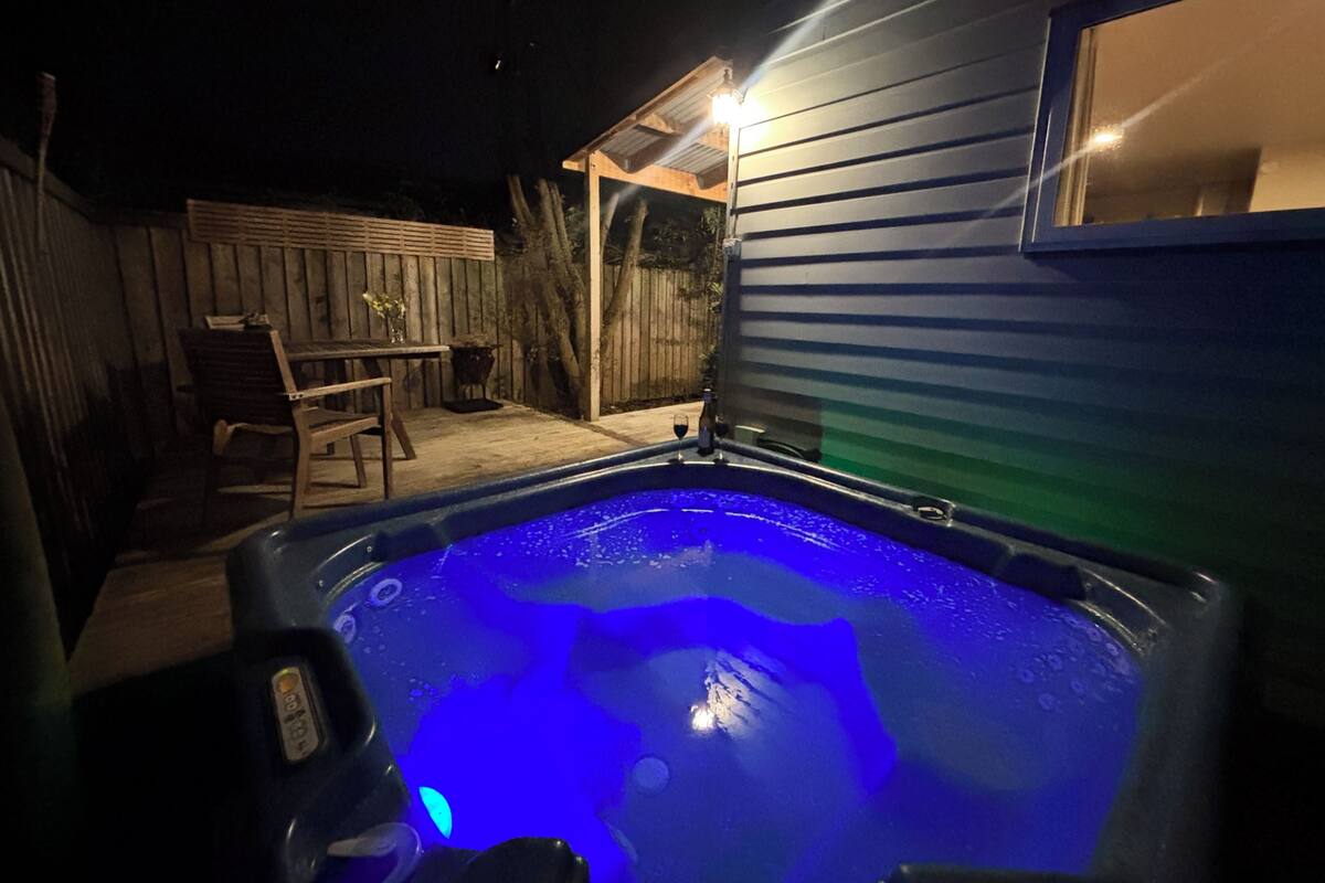 Una bañera de hidromasaje con luz azul, una terraza de madera y una valla de madera en un patio trasero.