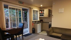 A compact hotel room with a bed, a desk with a chair, a kitchenette, and a sofa. - Cranford Cottages And Motel (Christchurch)