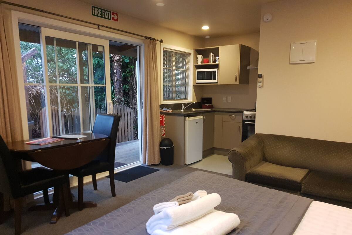 Una habitación de hotel compacta con cama, escritorio con silla, kitchenette y sofá.