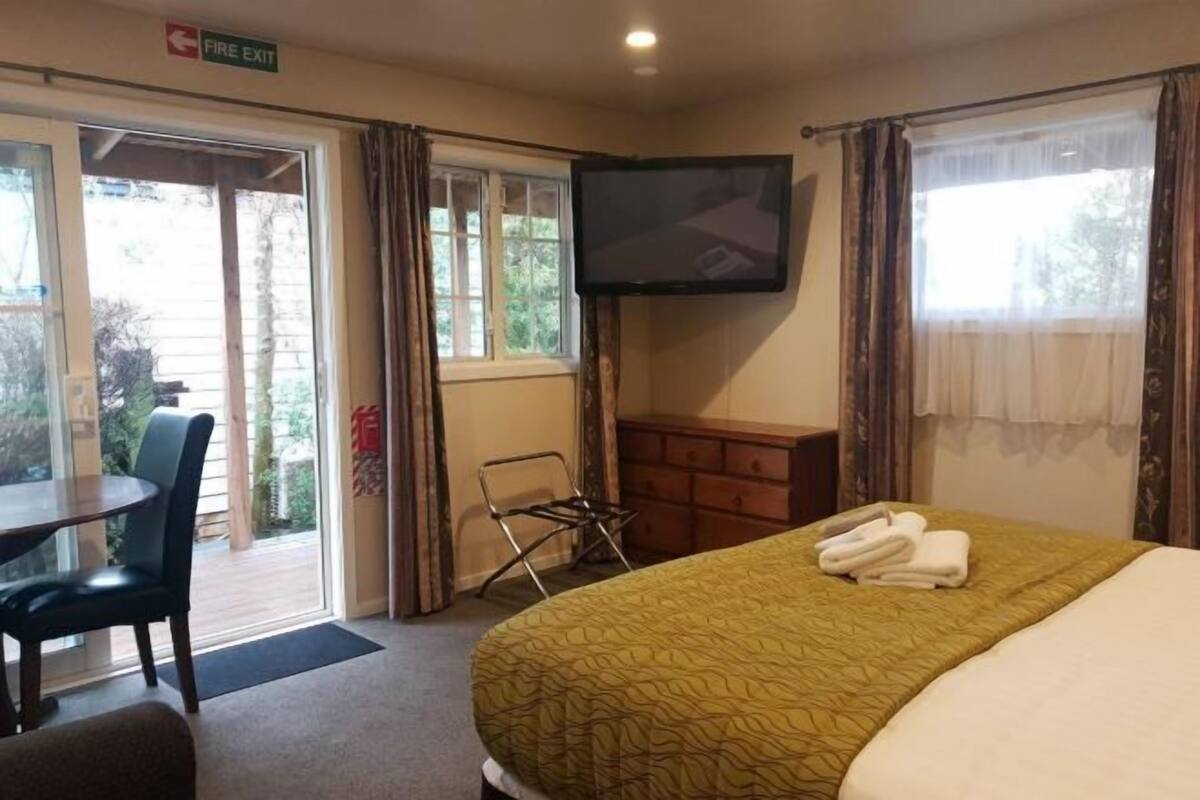 Una habitación de hotel con una cama, televisión, escritorio con silla y ventana.