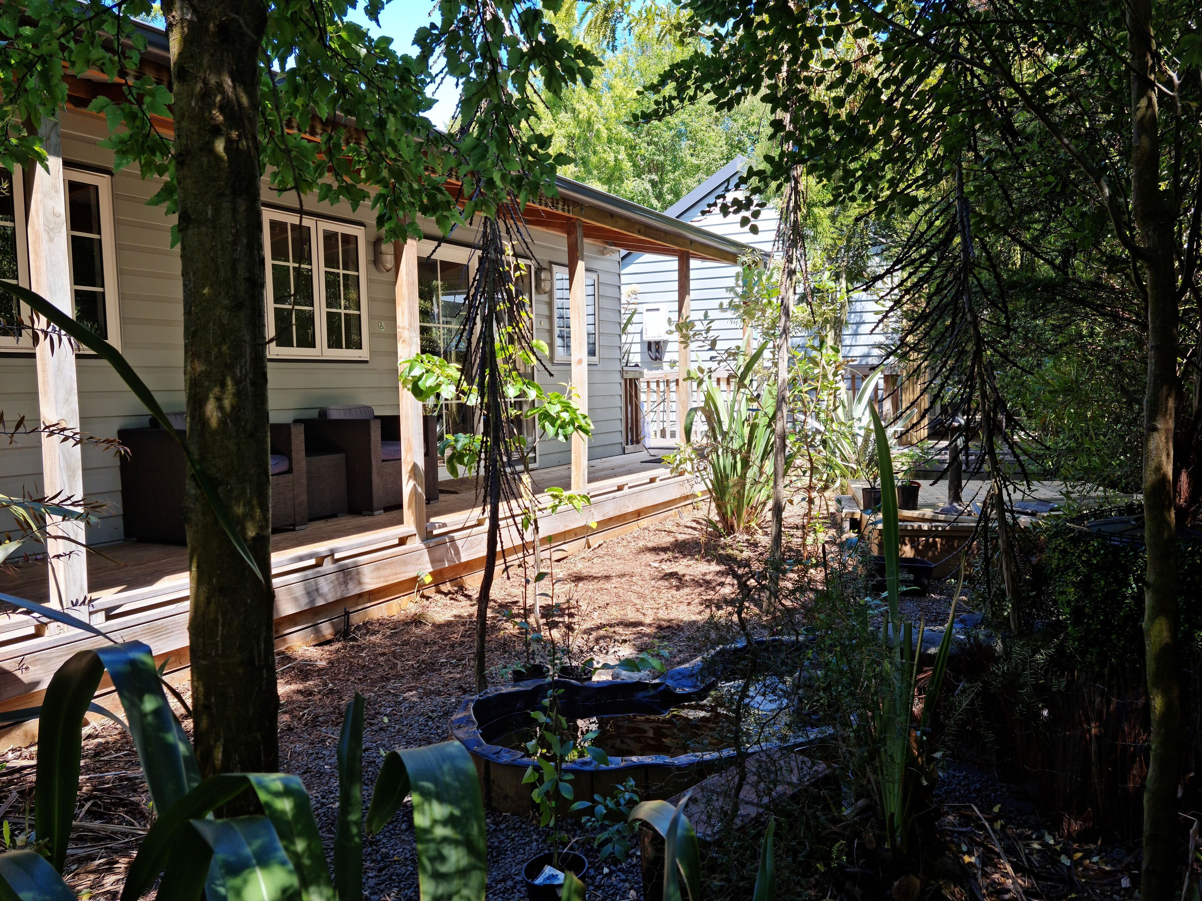 En boligejendom med en overdækket veranda, en lille have med et bassin og en træterrasse.