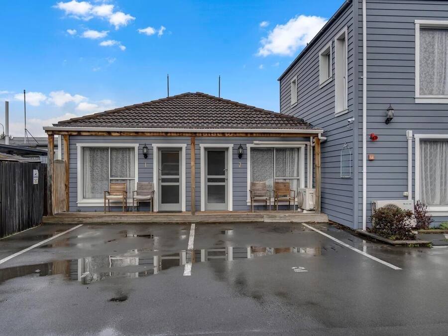 Un edificio a due piani con un portico coperto, un garage e un parcheggio.