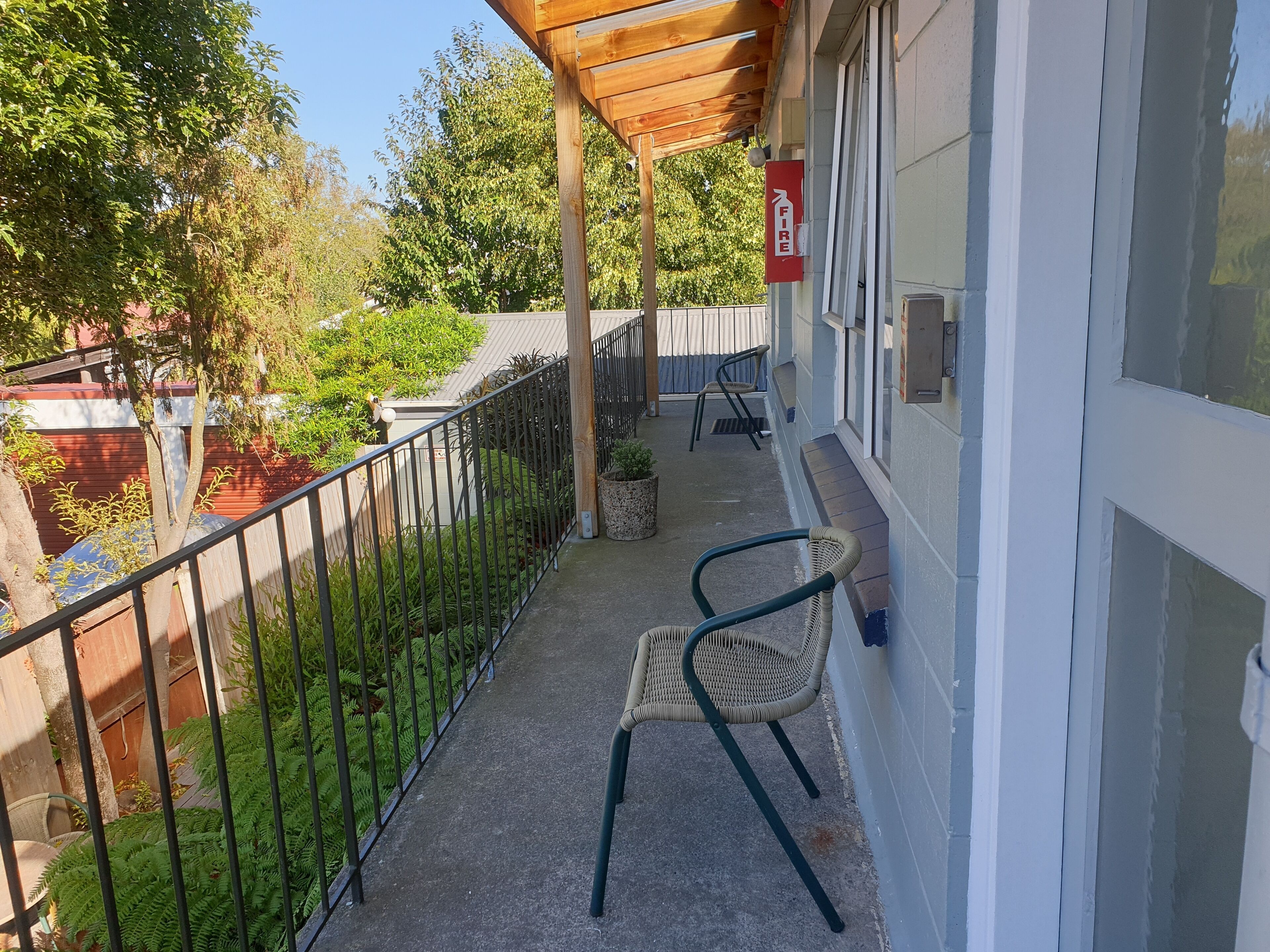 A balcony with a wooden pergola, a fire exit sign, a potted plant, and two wicker chairs.