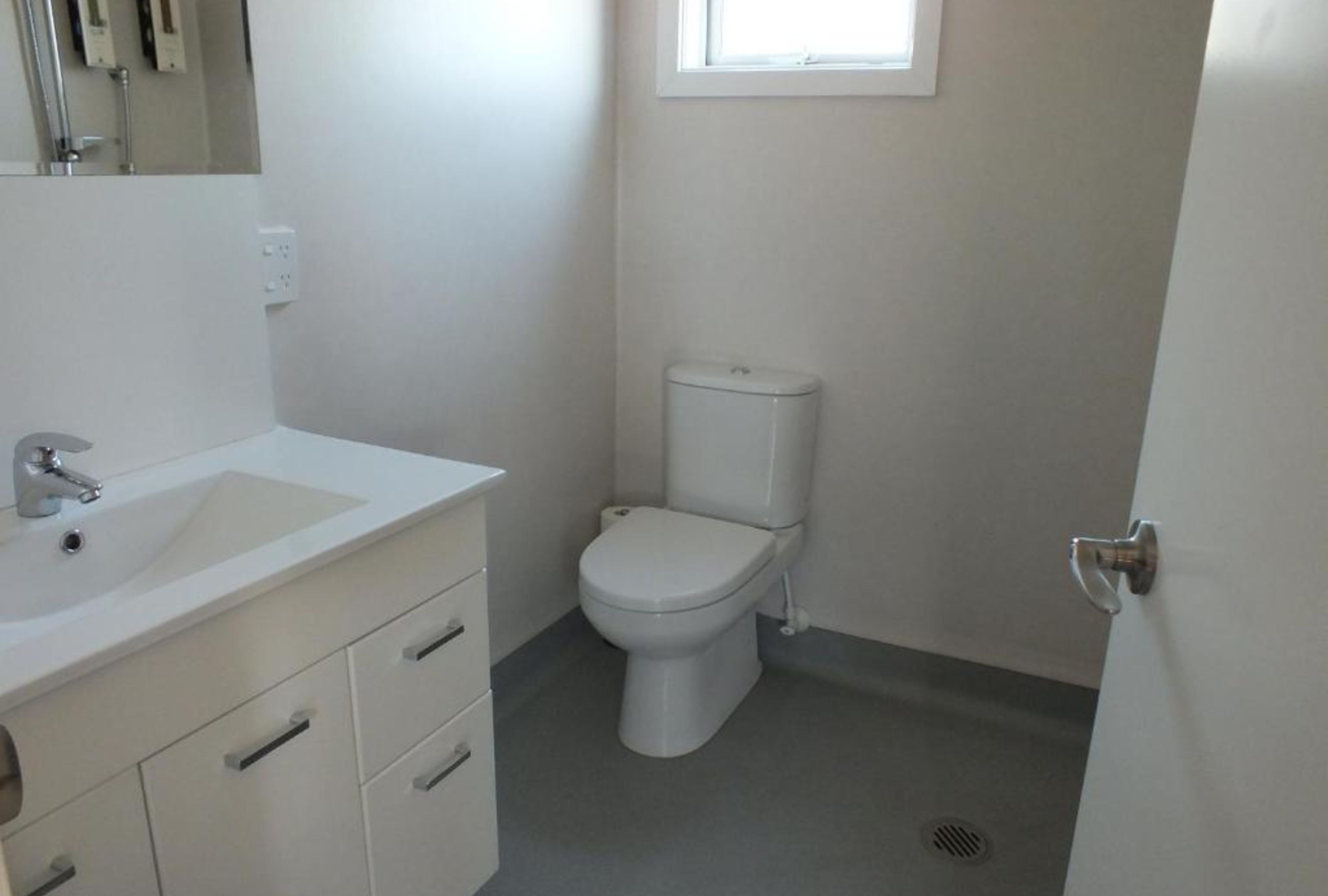 Un baño pequeño y limpio con un lavamanos blanco, un inodoro y una ventana sobre el inodoro.