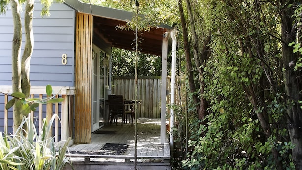 A wooden deck leading to a covered porch with a table and chairs, surrounded by dense greenery. - Cranford Cottages And Motel (Christchurch)