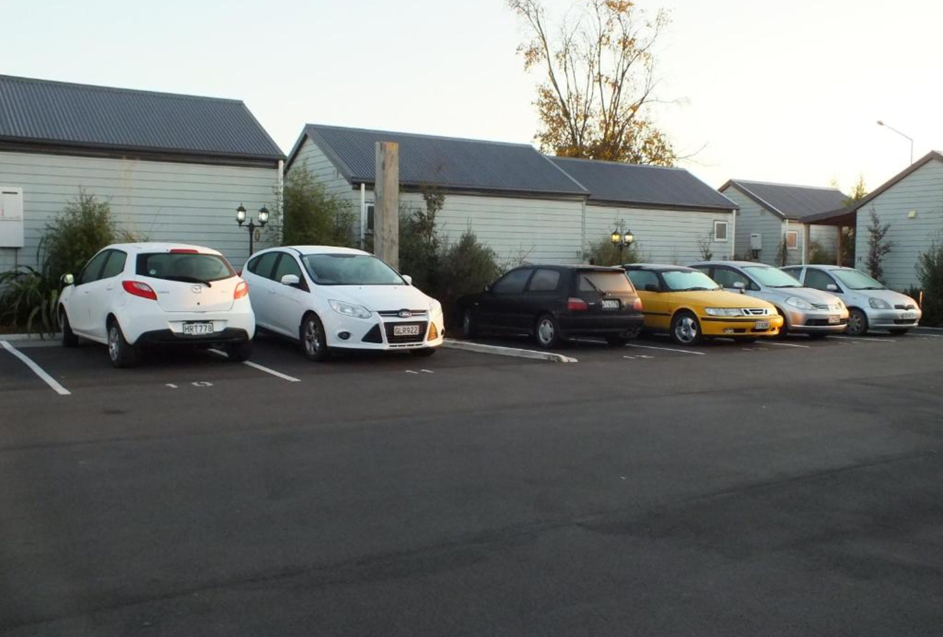 Un estacionamiento con varios coches aparcados frente a una hilera de casas.