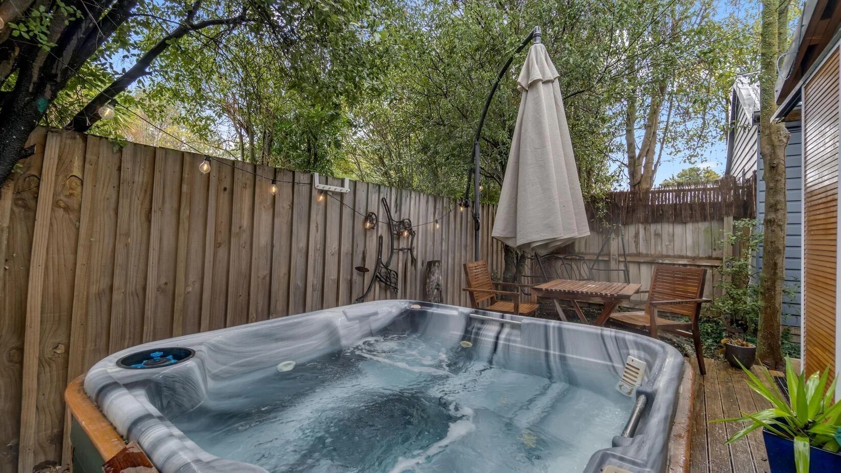 A hot tub in a backyard with a wooden fence, outdoor furniture, and a pergola.
