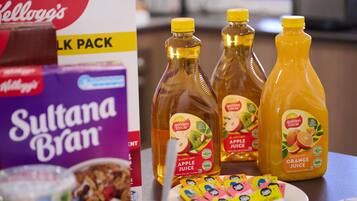 Una mesa con alimentos, incluyendo un paquete de leche, zumo de manzana y botellas de zumo de naranja.