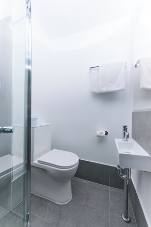 Un baño moderno con cabina de ducha de vidrio, inodoro blanco, lavabo y toallero.