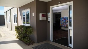A building entrance with a door, a small bush, a sign, and a wall-mounted device. - Ibis Budget Perth Airport (Redcliffe)
