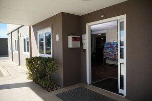 Entrada de un edificio con una puerta, un arbusto pequeño y un cartel en la pared.