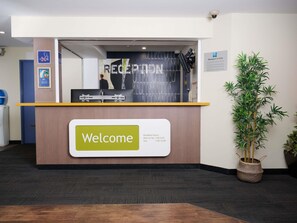 Ein Empfangsbereich mit einem ‚Welcome‘-Schild, einer Pflanze und einem Schild ‚Verantwortliche anwesend‘.