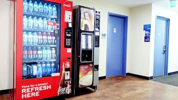 A vending machine area with Coca-Cola and Nescafé machines, a public toilet sign, and a blue door.