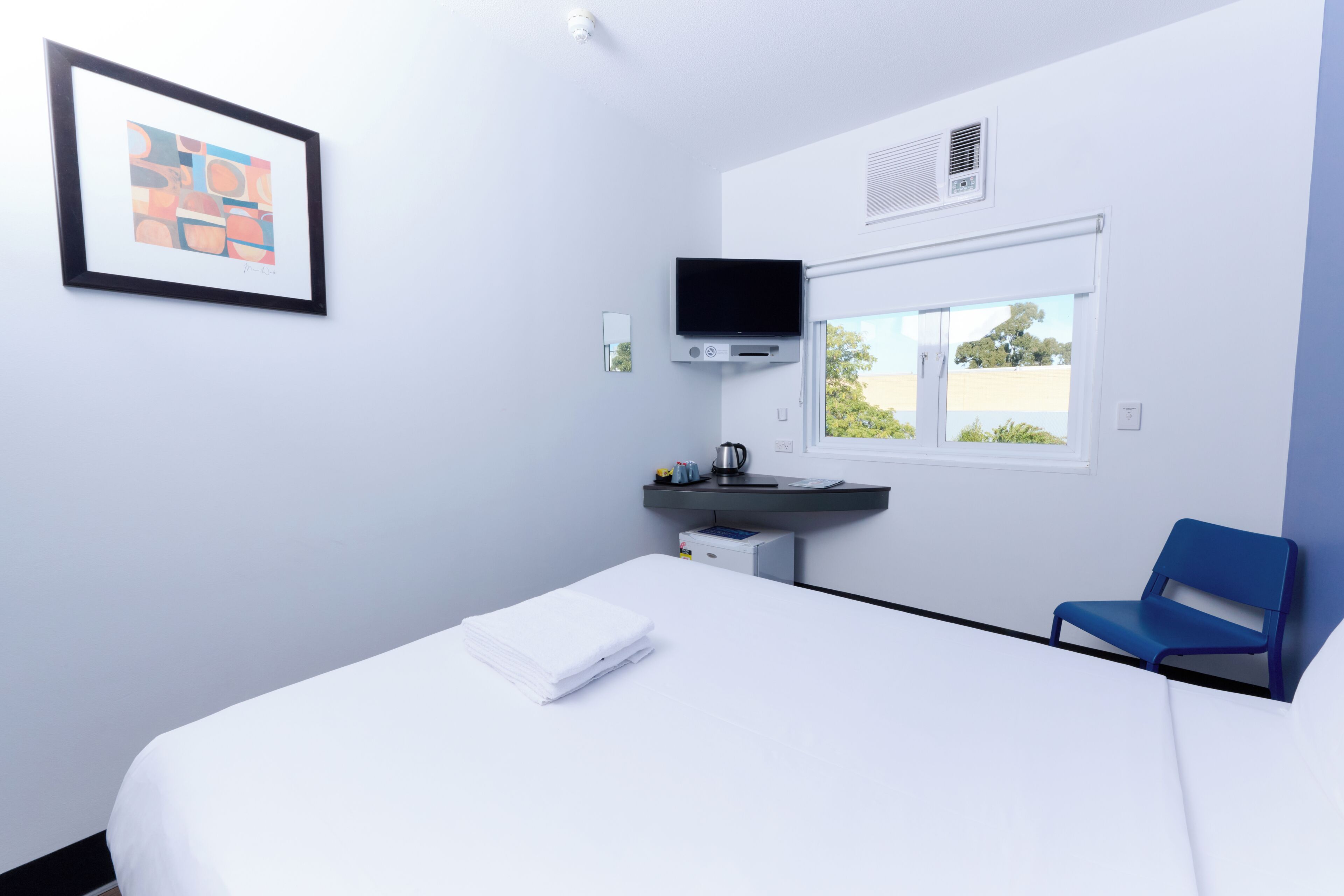 A hotel room with a bed, a desk with a flat-screen TV, a chair, and a window with a view.