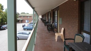 Un espacio al aire libre cubierto con mesas y sillas, una pared de ladrillo y vistas a coches aparcados y edificios al fondo.