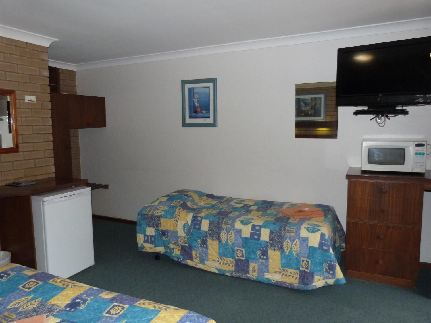 A small, simple room with a bed, a refrigerator, a microwave, and a television.