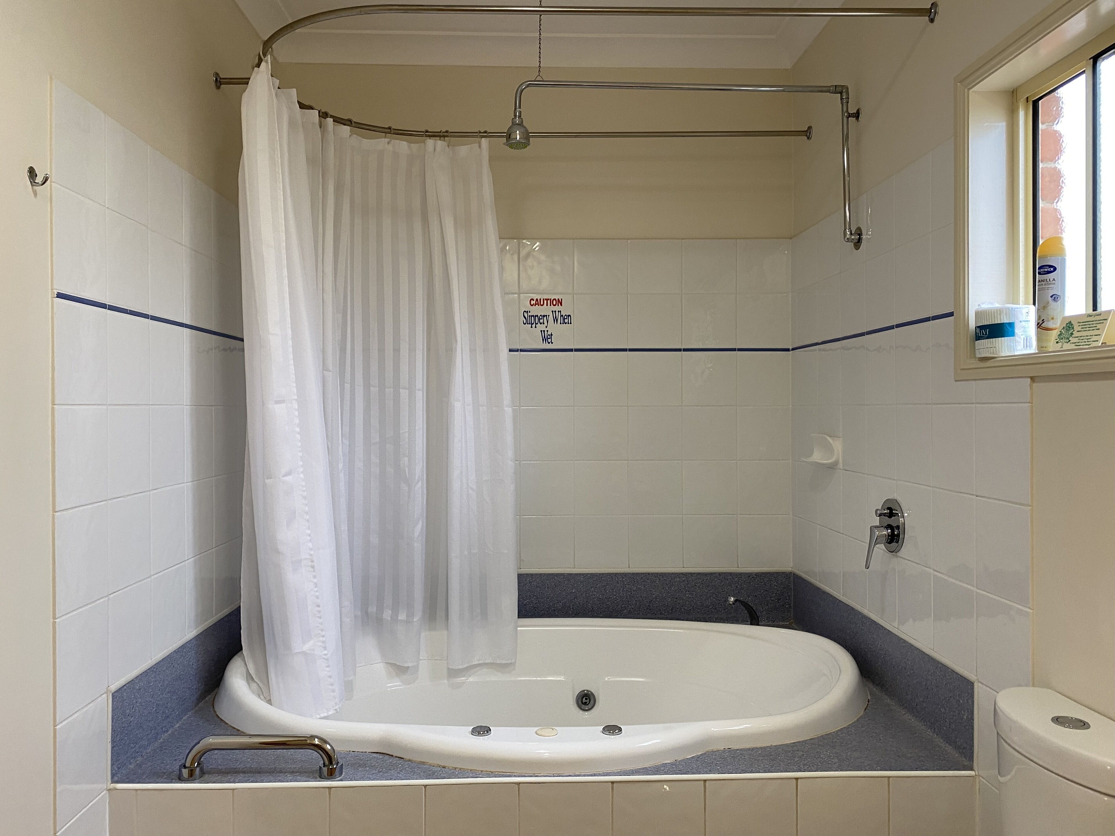A bathroom with a bathtub, a shower curtain, and a caution sign.