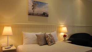 Une chambre d’hôtel avec un lit, deux lampes de chevet, une table de chevet avec un téléphone, une chaise, un tableau au mur et un vase avec des fleurs.