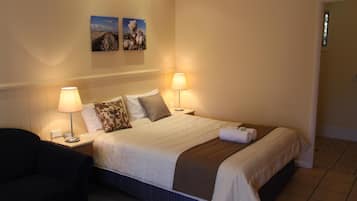 Una camera d'albergo ordinata con un letto, due lampade ai comodini, una sedia e due quadri appesi al muro.