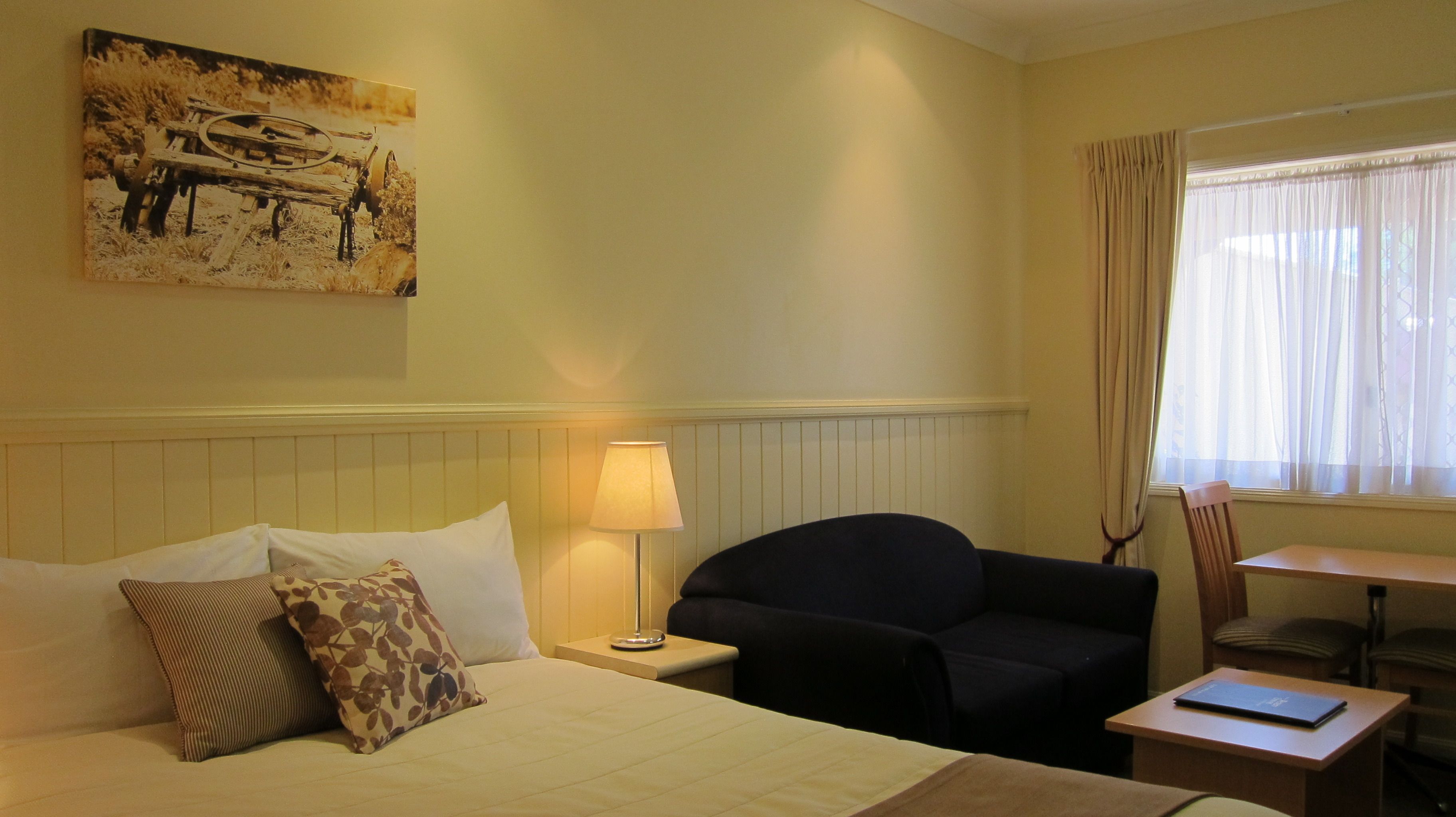 Una habitación de hotel con cama, una silla, un escritorio, una lámpara y un cuadro en la pared.