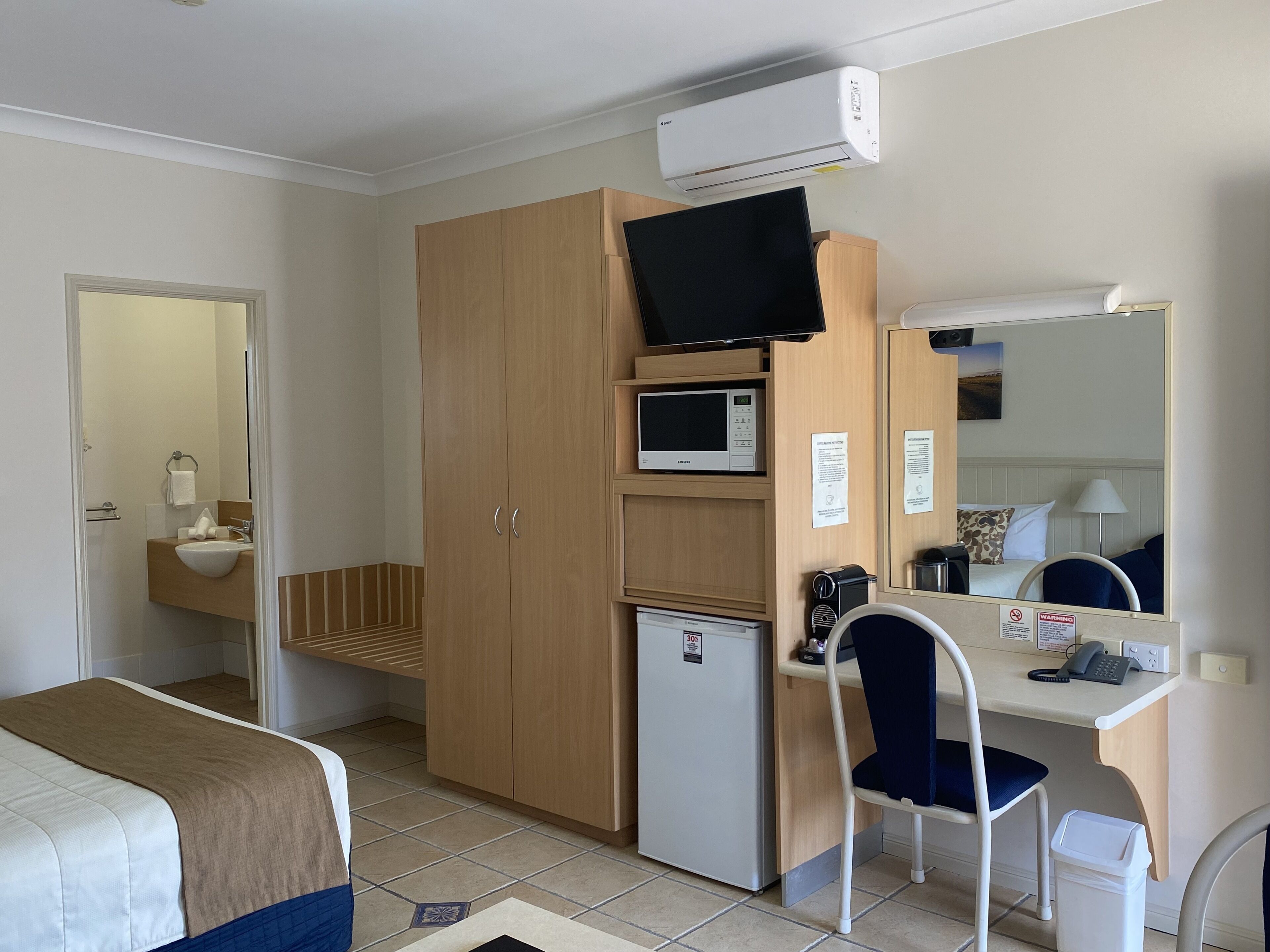 Une chambre d’hôtel comprenant un lit, un bureau avec une chaise, un four à micro-ondes, un réfrigérateur, une télévision et une salle de bain visible à travers une porte ouverte.