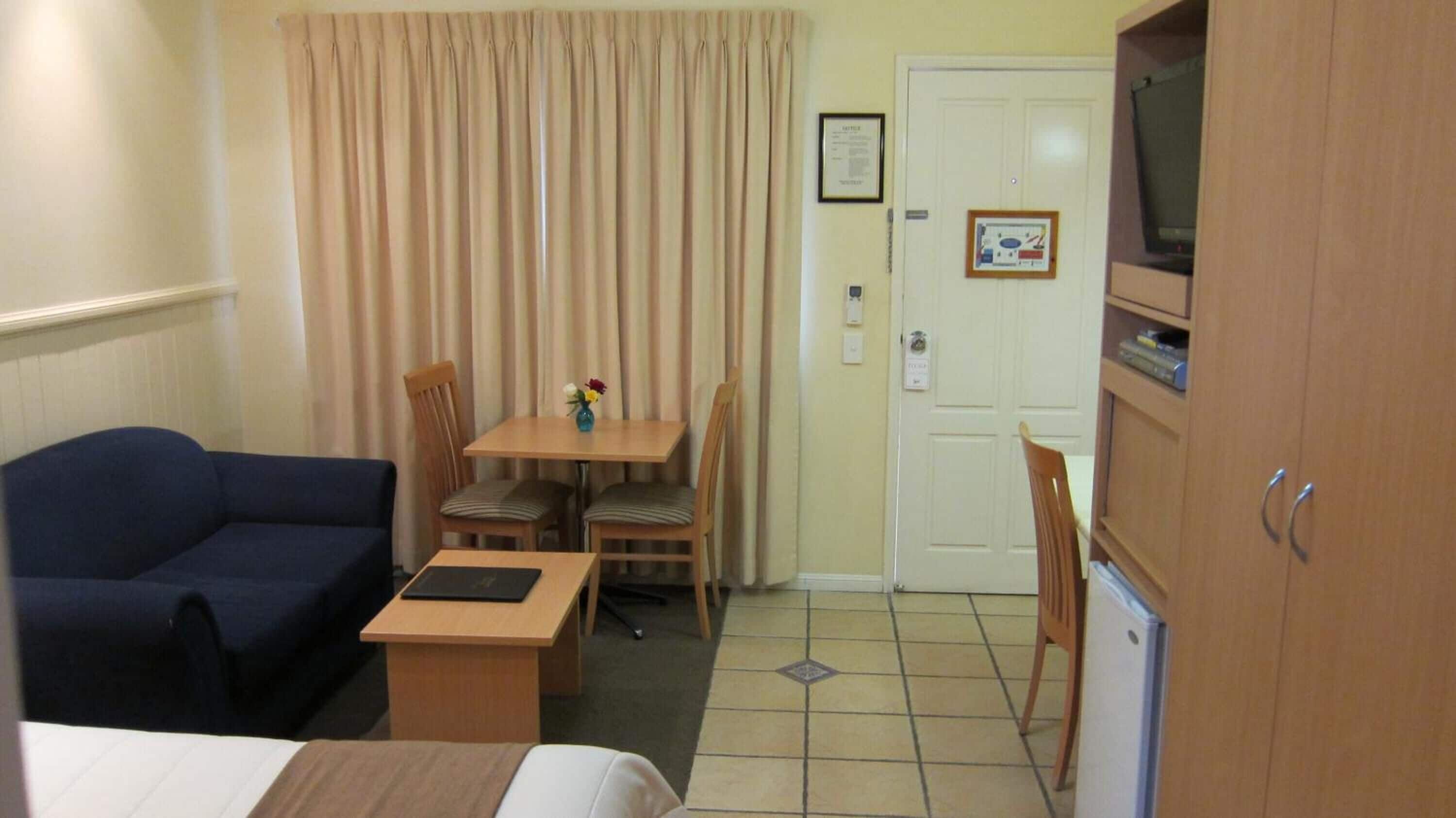 A hotel room with a bed, a blue sofa, a wooden table with chairs, a television, and a door with a sign.