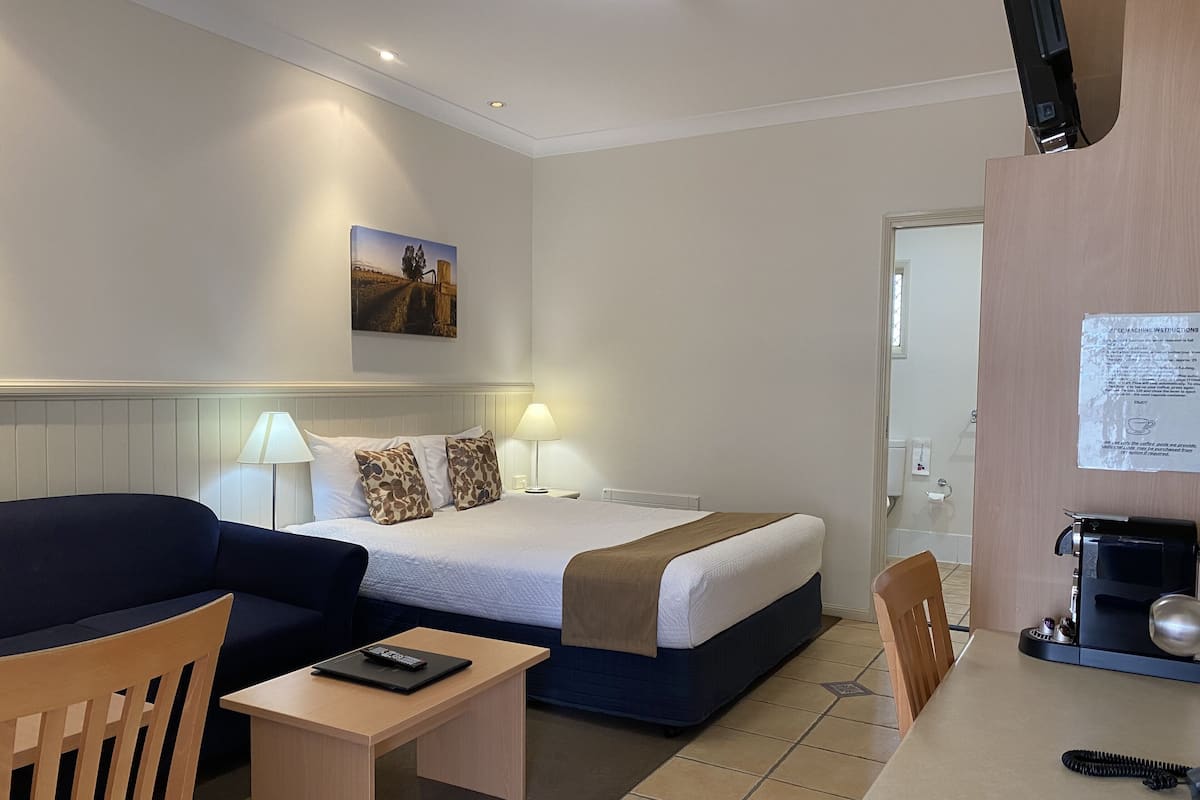 A hotel room with a bed, a desk, a chair, a lamp, and a coffee machine.