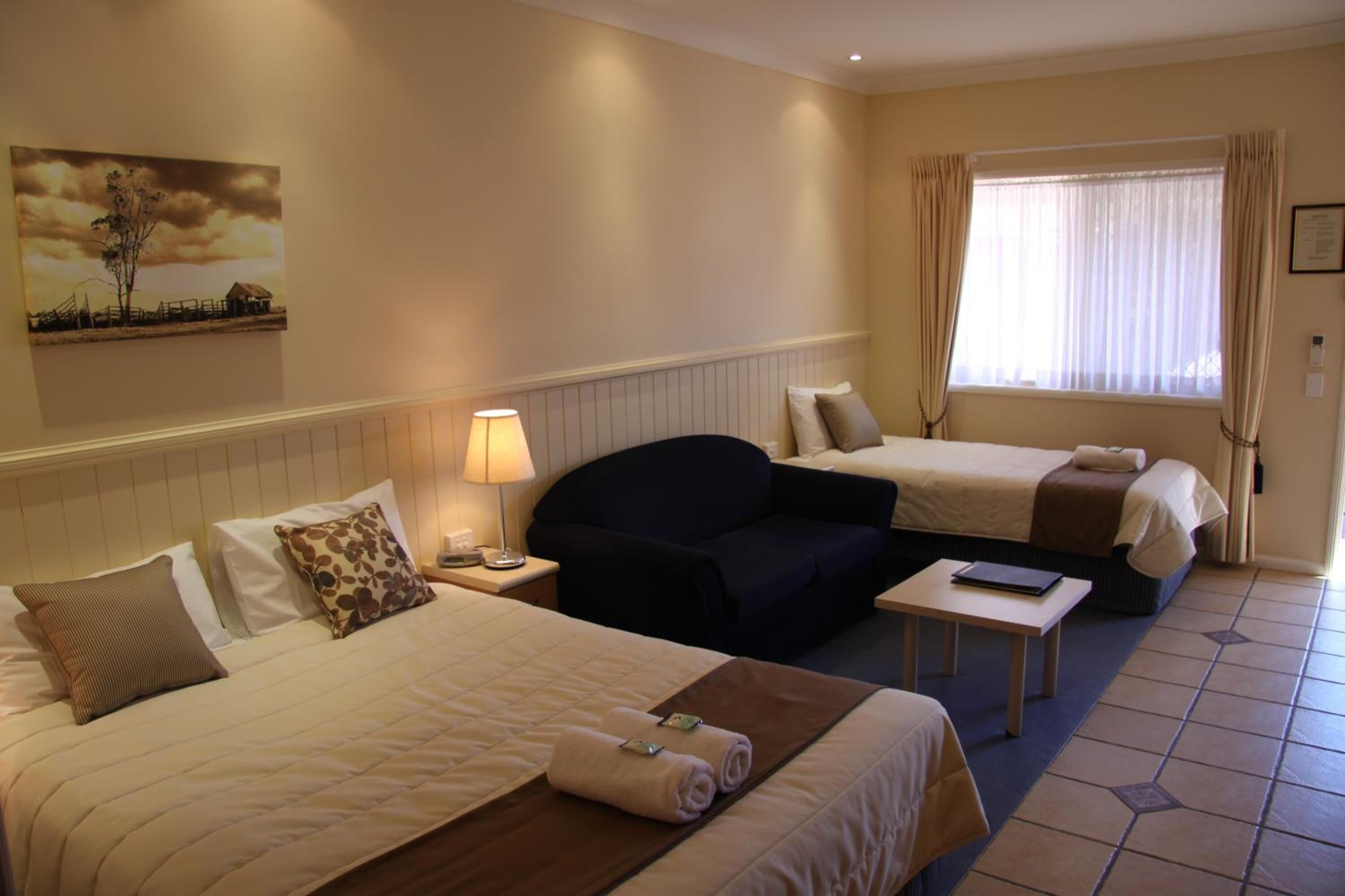 Ein Hotelzimmer mit zwei Betten, einem Schlafsofa, einem kleinen Tisch und einem Bild an der Wand.