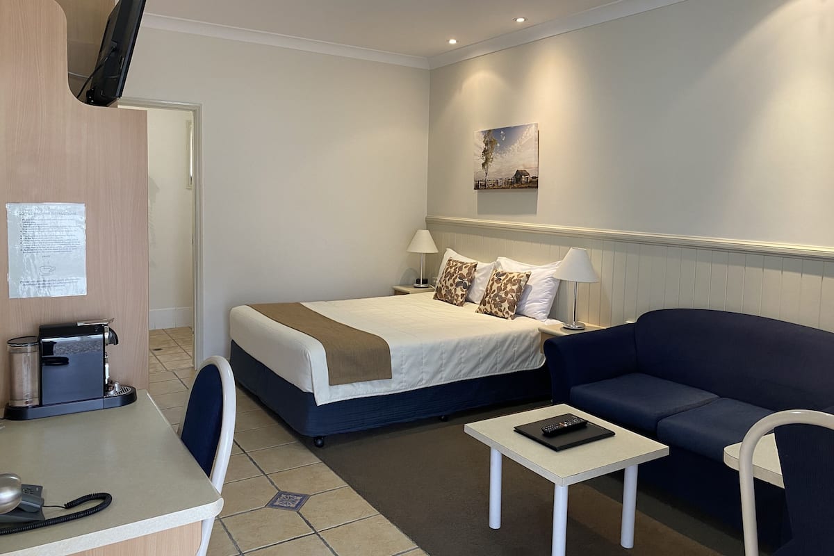 A hotel room with a bed, a sofa, a small table, a desk with a phone, and a coffee machine.