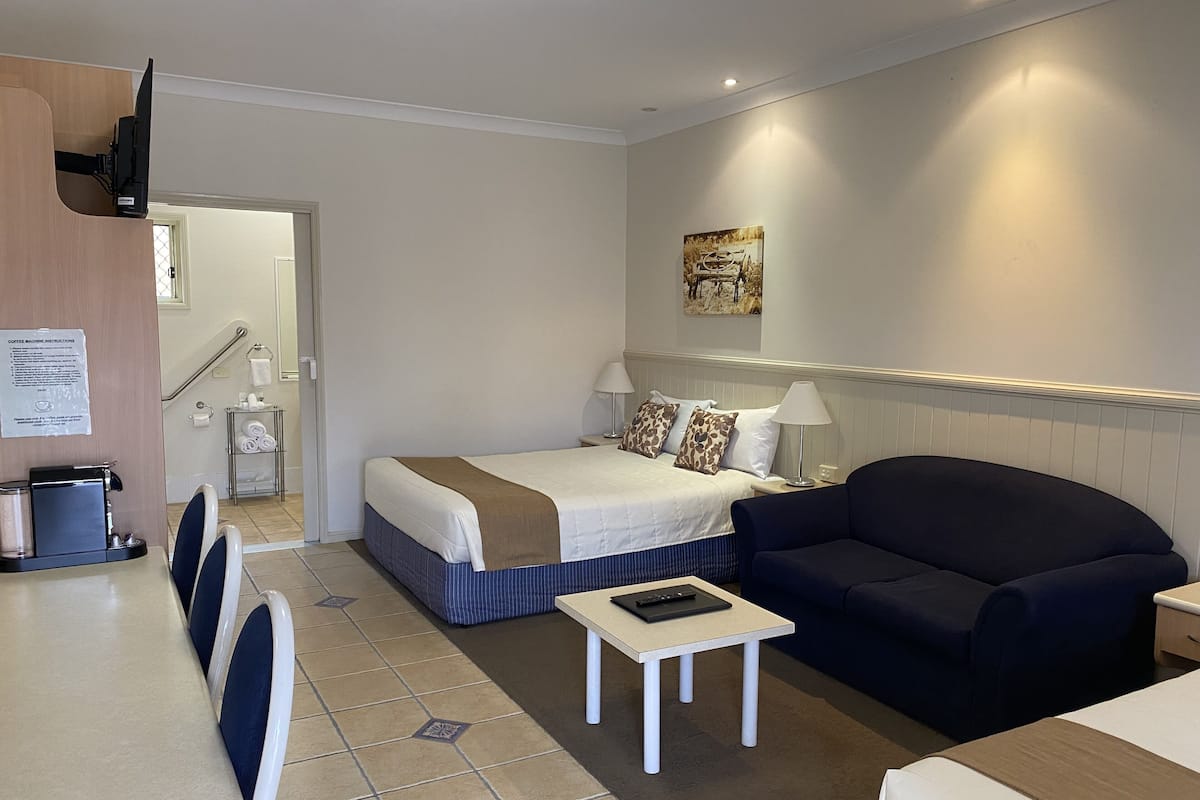 A hotel room with a bed, a sofa, a small table, a coffee machine, and a TV.