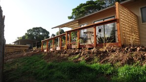 Una casa moderna con terraza de madera, ventanas amplias y un muro de contención de piedra.