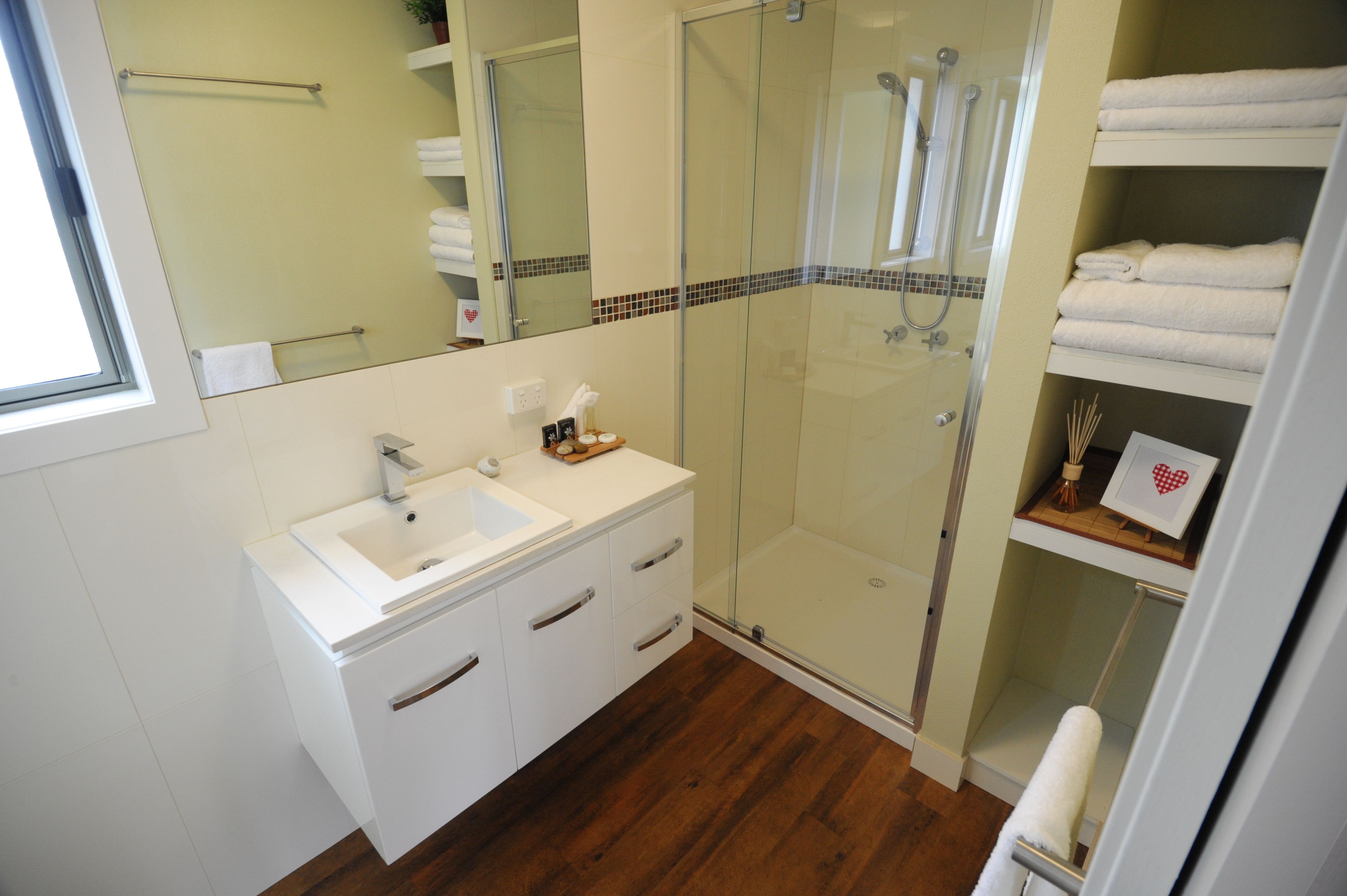 A modern bathroom with a glass-enclosed shower, white vanity with a sink, and neatly folded towels on shelves.