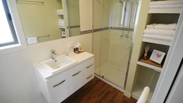 A modern bathroom with a glass-enclosed shower, white vanity with a sink, and neatly folded towels on shelves.