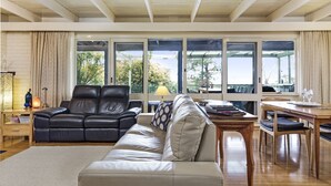 Un salón amplio con sofá de cuero, una mesa de comedor de madera y grandes ventanales con vistas al exterior.