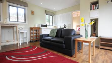 A modern living room with a black leather sofa, a red rug, a wooden coffee table, and a kitchen area in the background.