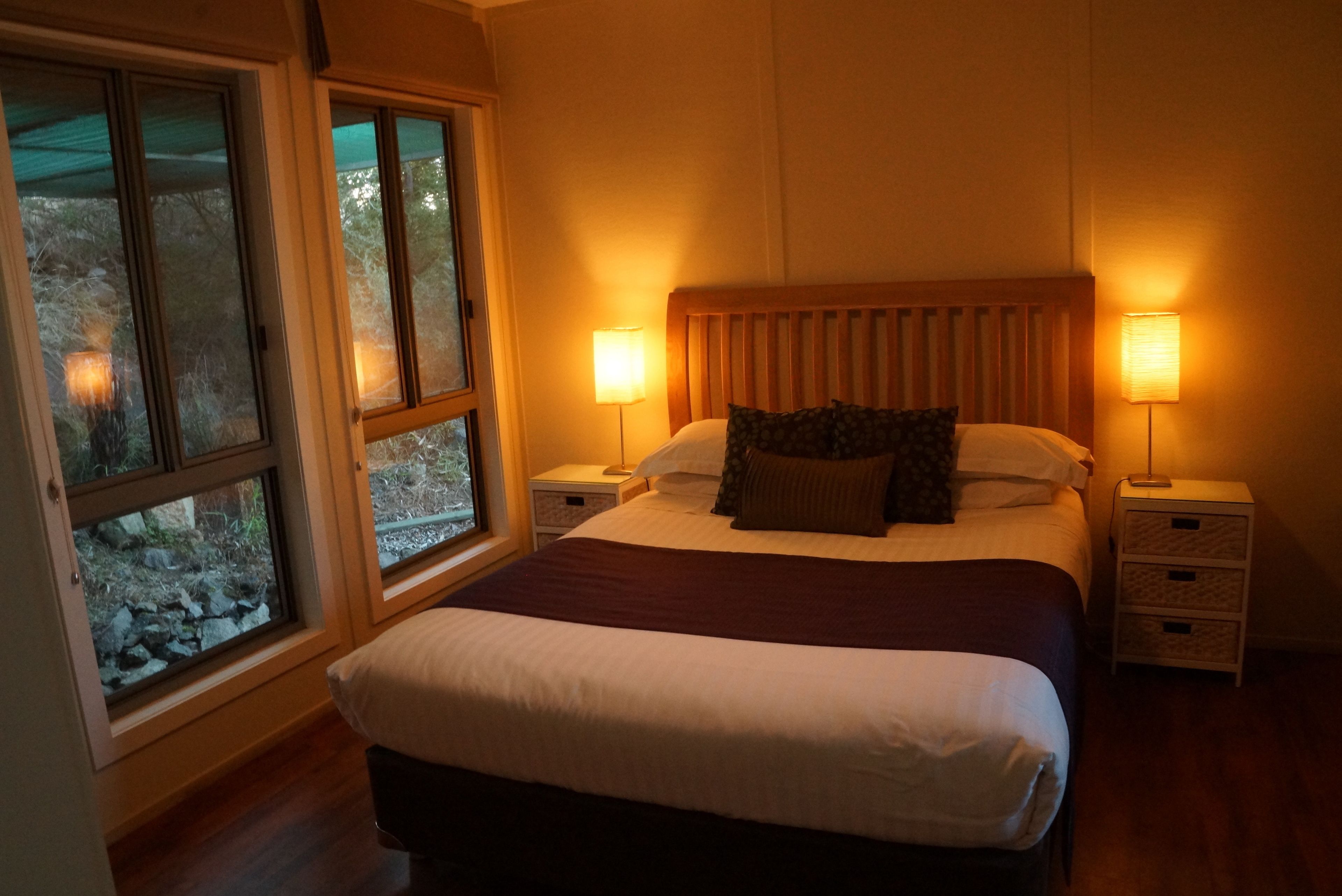 Ein Schlafzimmer mit einem großen Bett, zwei Nachttischen und einem Fenster mit Blick auf Bäume.