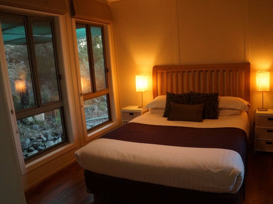 Un dormitorio con una cama grande, dos mesitas de noche y una ventana con vistas a árboles.