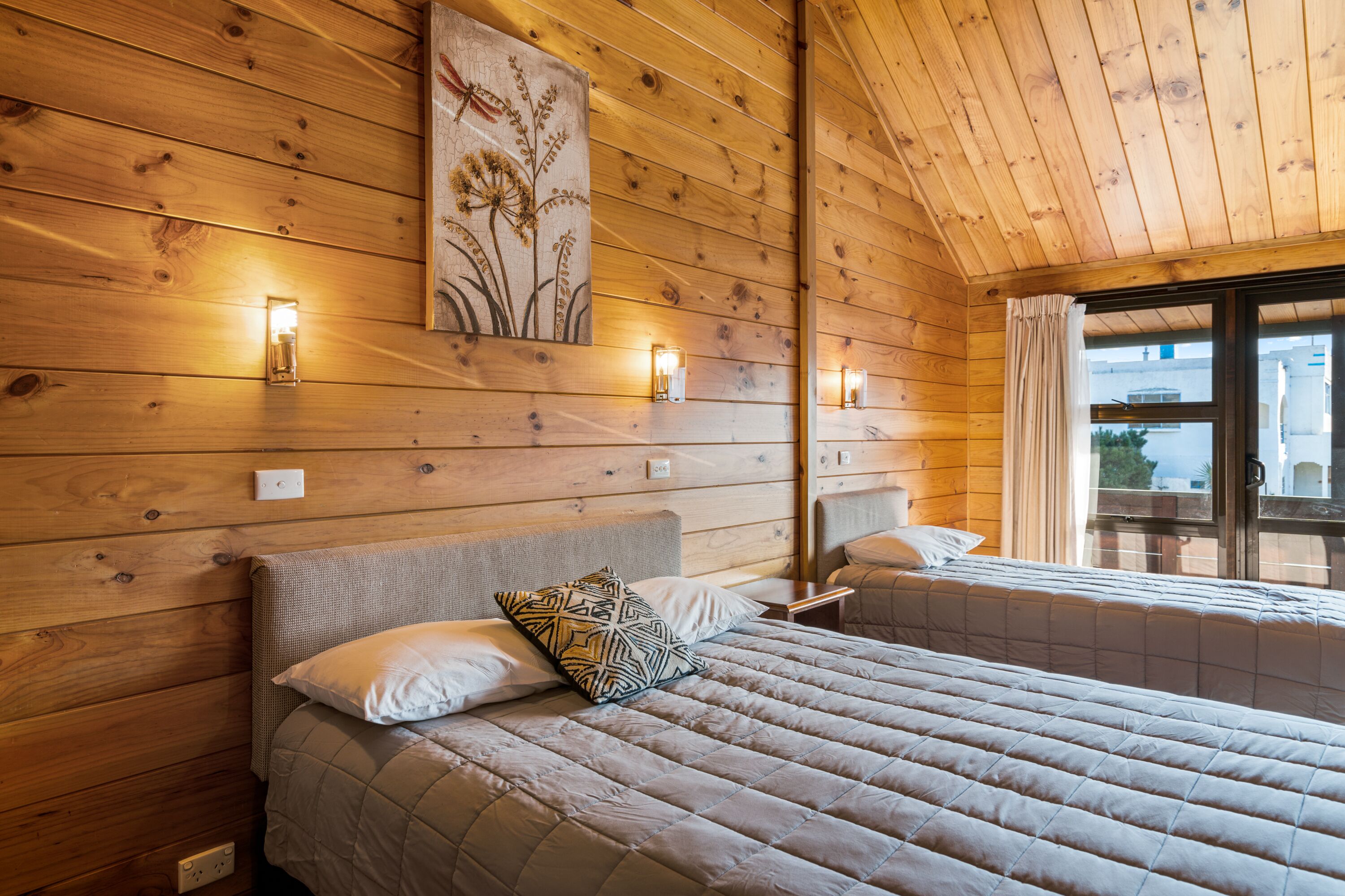 A wooden-paneled room with a bed, bedside tables, and wall-mounted lights.