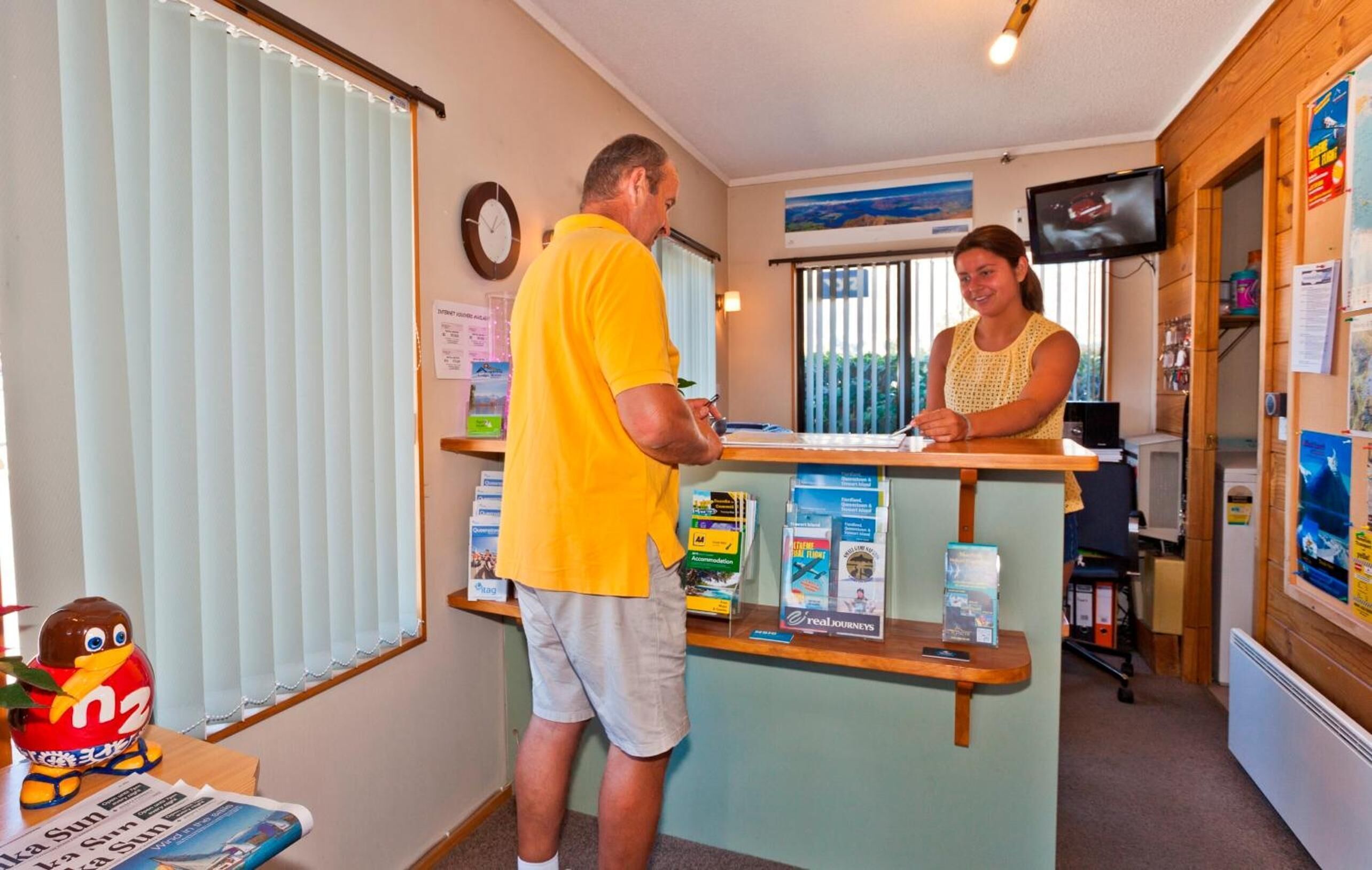 A reception desk with a man and a woman, a clock, a television, and various informational brochures.