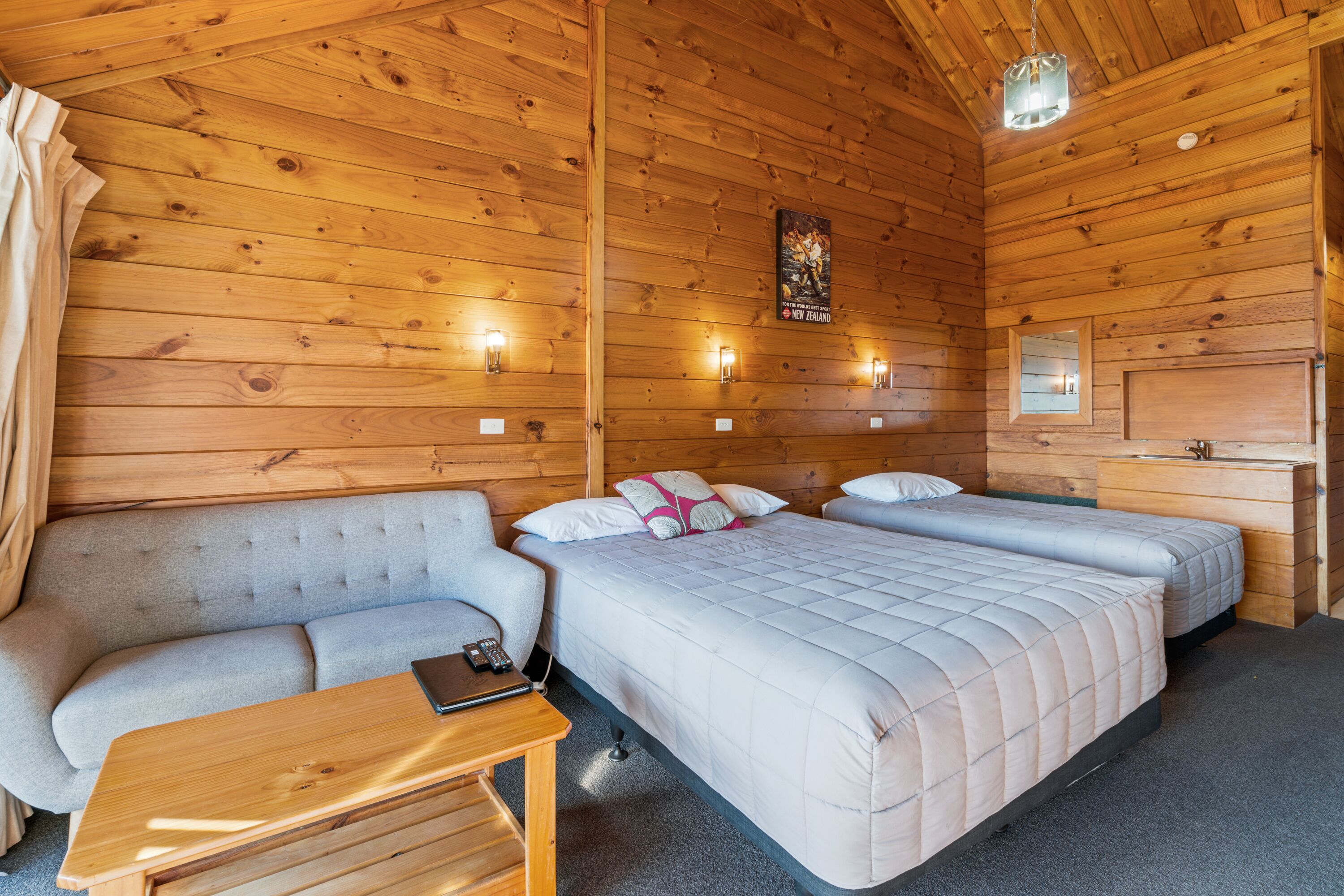 A wooden cabin room with a sofa, two beds, a small table, and a mirror.