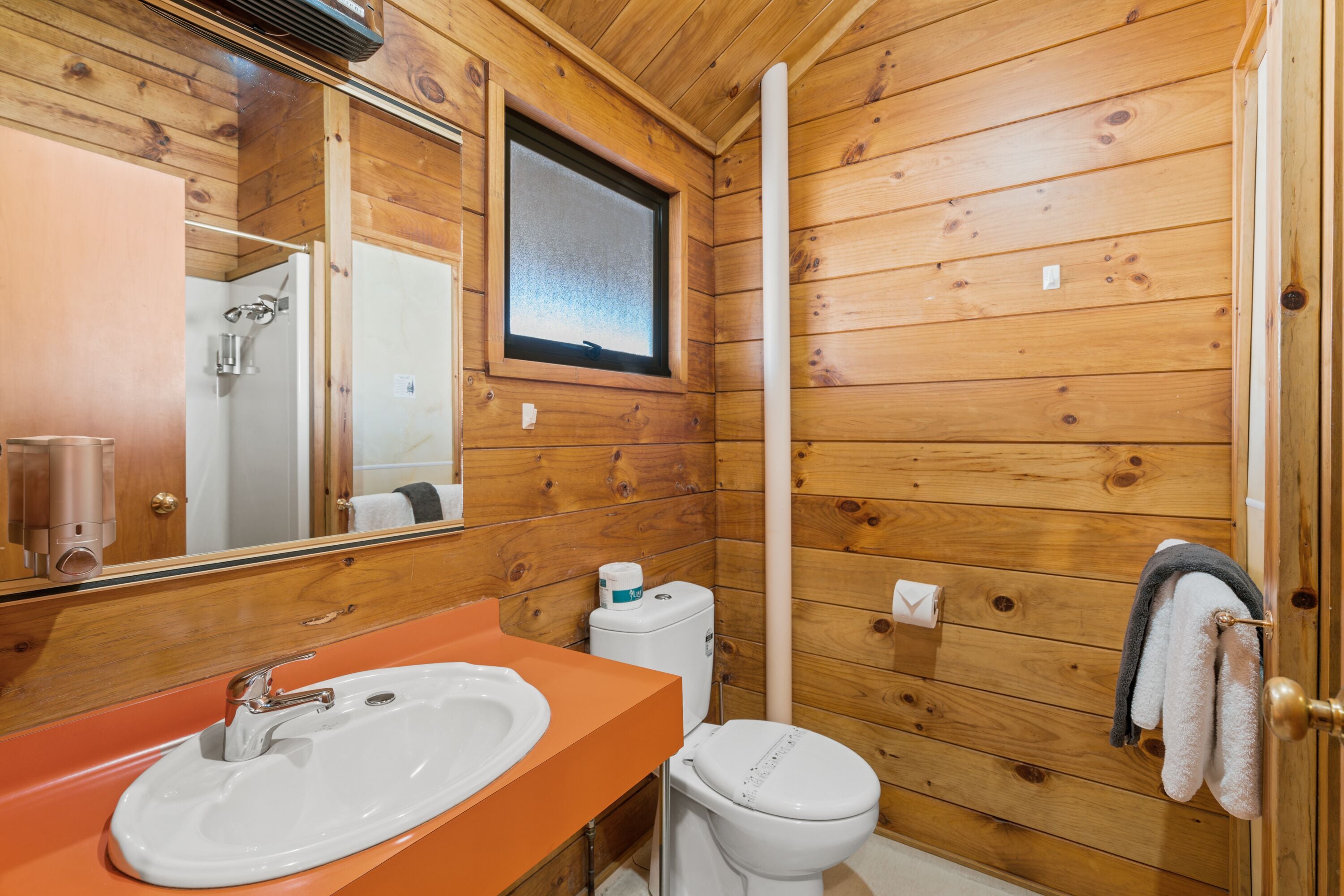Un baño con paneles de madera, un lavabo, un inodoro y una ventana.