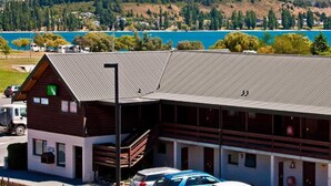 Een lodge met een houten gevel en een metalen dak, gelegen bij een meer met bergen op de achtergrond.