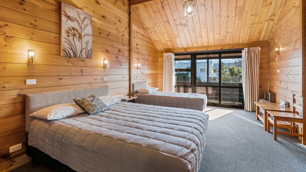 Een houten slaapkamer met twee bedden, een eethoek en een grote schuifdeur naar buiten.