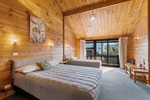 Une chambre aménagée dans une cabane en bois, avec deux lits, un coin repas et une grande porte-fenêtre coulissante donnant sur l’extérieur.
