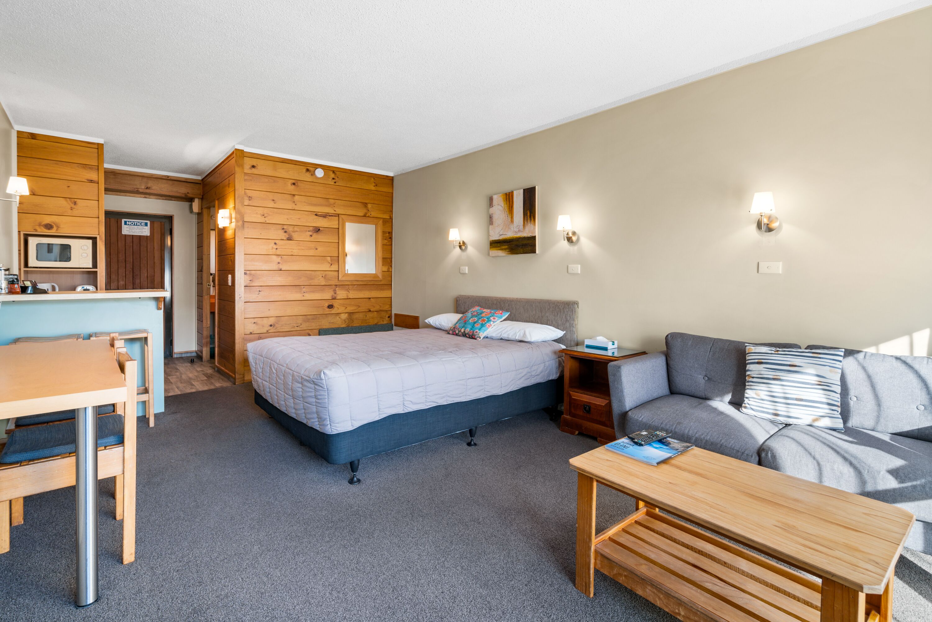 A compact room with a bed, a sofa, a small table, a desk, and a microwave.